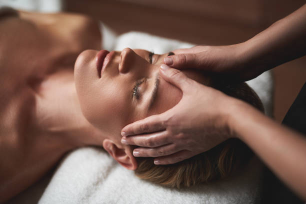 Concept of relaxation and body care. Top angle portrait of female therapist making anti-age massage of forehead wrinkles to young woman in spa salon