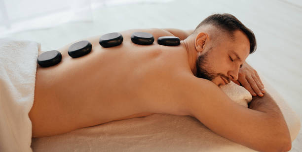 Handsome man at spa resort receive hot stone massage. Speciality massage using smooth, heated stones